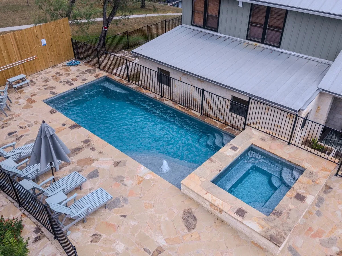 Latham Olympia 14 pool with a tanning ledge, bubbler, raised spa, and stone patio at Lake McQueeney, Texas.